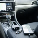 Migliori adattatori Android Auto wireless provati su strada posati sul tunnel centrale di un'auto di fianco a uno smartphone, con lo schermo dell'infotainment che mostra Android Auto attivo.