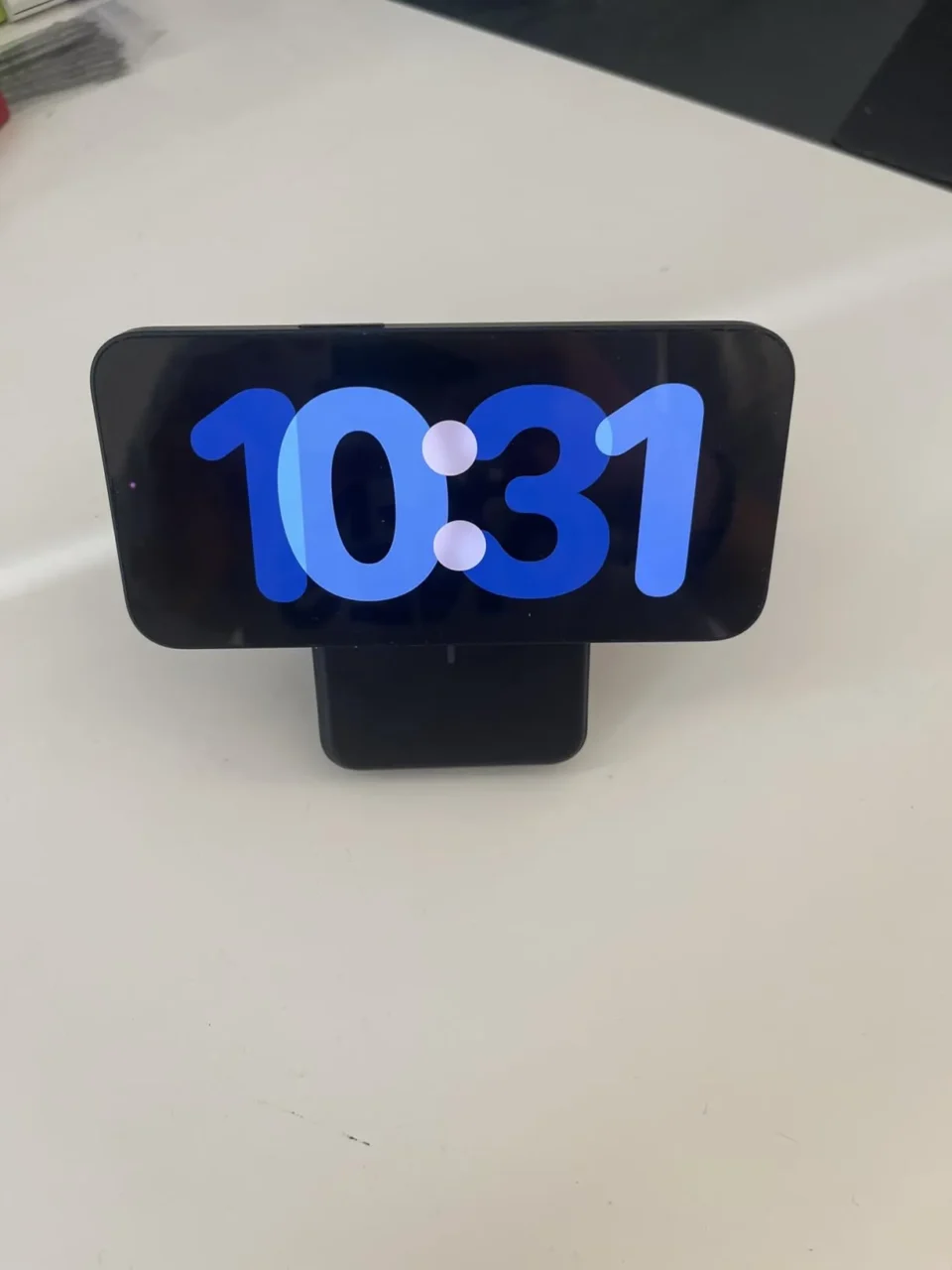 iPhone appoggiato orizzontalmente su una base di ricarica magnetica nera, con display acceso sull'orologio, tra i migliori accessori tech 2026.