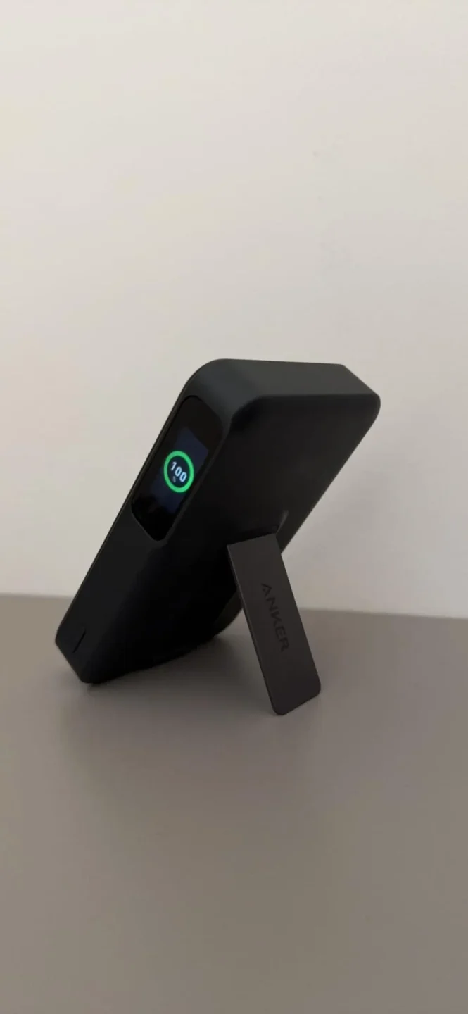 Vista laterale di un power bank Anker nero con kickstand aperto e display digitale che segna il 100% di batteria, tra i top accessori tech 2026.