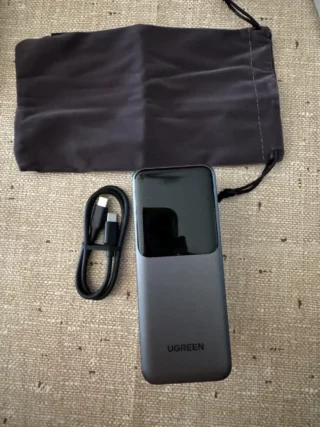 I 4 Migliori Powerbank per Viaggiare (2026): Guida e Regole Volo 16 Power bank UGREEN grigio siderale con display digitale, cavo USB-C e custodia in velluto grigio su superficie testurizzata.