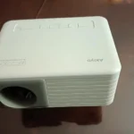 Proiettore 4K economico Akiyo O1 di colore bianco visto dall'alto, appoggiato su un tavolo lucido, con i pulsanti di controllo in evidenza.