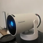 Proiettore 4K economico Magcubic HY300 Pro acceso su un mobile, con lente illuminata in ambiente domestico.