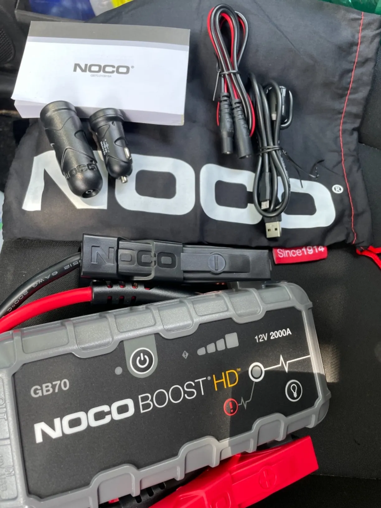 Avviatore emergenza auto NOCO Boost HD GB70 da 2000A con accessori, cavi e custodia protettiva in mostra sui sedili dell'auto.